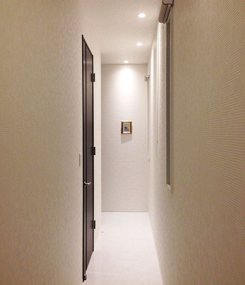 玄関に立つと、長い廊下が現れる。「キッチン、洗面所、トイレに直行できる動線を作りつつ、廊下に面積を割くことで贅沢な空間にしました。廊下のダウンライトは壁に反射する光の角度を考えて、配置しました」